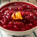 A white ceramic bowl filled with cranberry sauce, on a striped tablecloth.