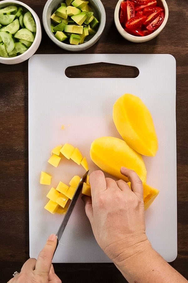 cutting mango chunks on a white chopping board.