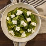 white ceramic bowl with rigatoni pasta, which is coated in a bright green kale sauce and dotted with ricotta cheese