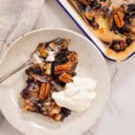 Blueberry and pecan baked oatmeal, scooped onto a white plate and served with a dollop of thick yogurt. A fork sits on the plate, and a beige napkin alongside.