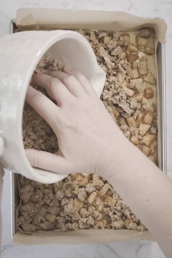 Hand sprinkling crumb topping over diced apples in a baking pan.