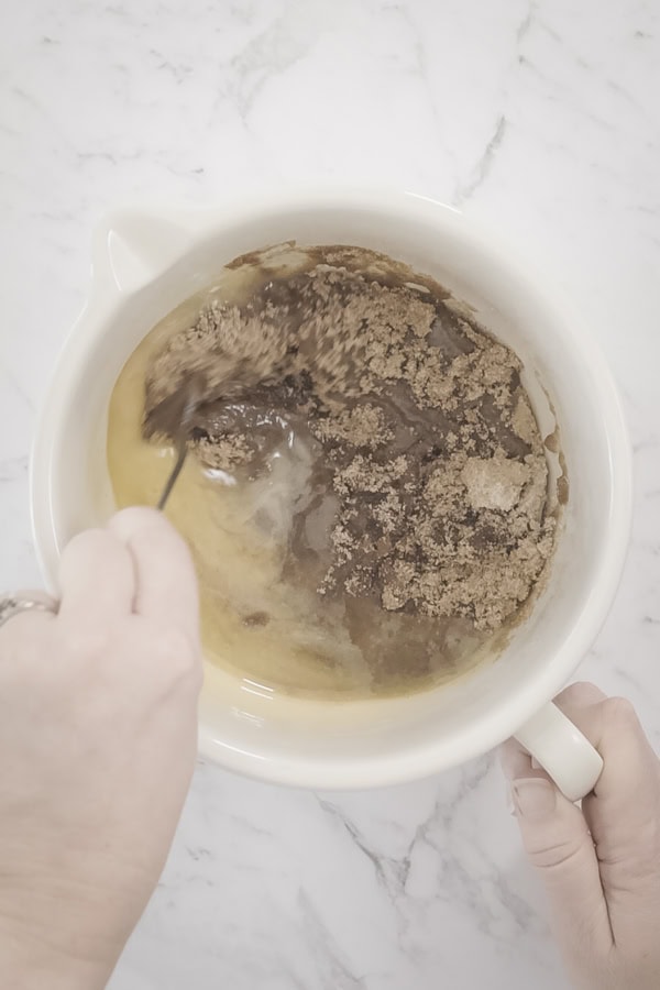 Stirring brown sugar and melted butter in a white bowl for apple crumb cake topping.