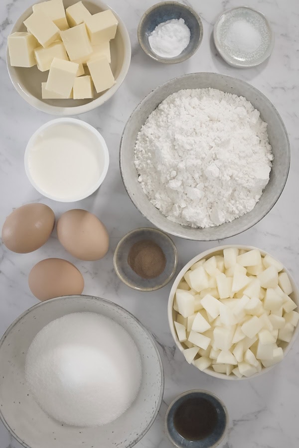 Ingredients for the apple crumb cake base and filling arranged in small bowls on a marble surface.