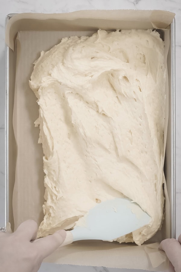 Spreading apple crumb cake batter into a lined baking pan with a spatula.