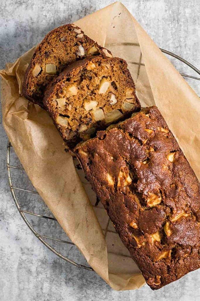 A top-down view of apple walnut bread; the loaf sits on brown paper and two slices are cut from the end, with the sliced cross sections visible in shot.