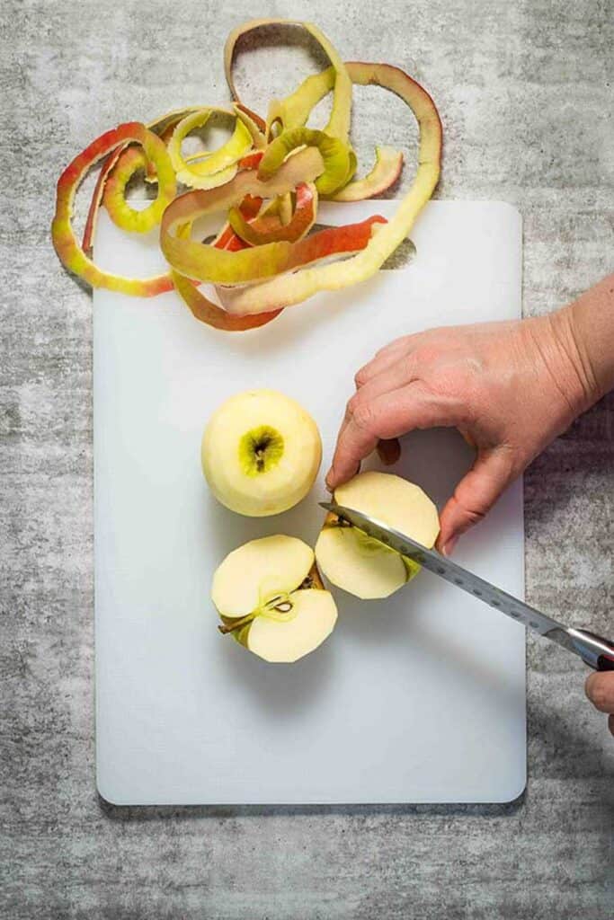 Peeling and chopping apples for apple and walnut bread, on a white chopping board