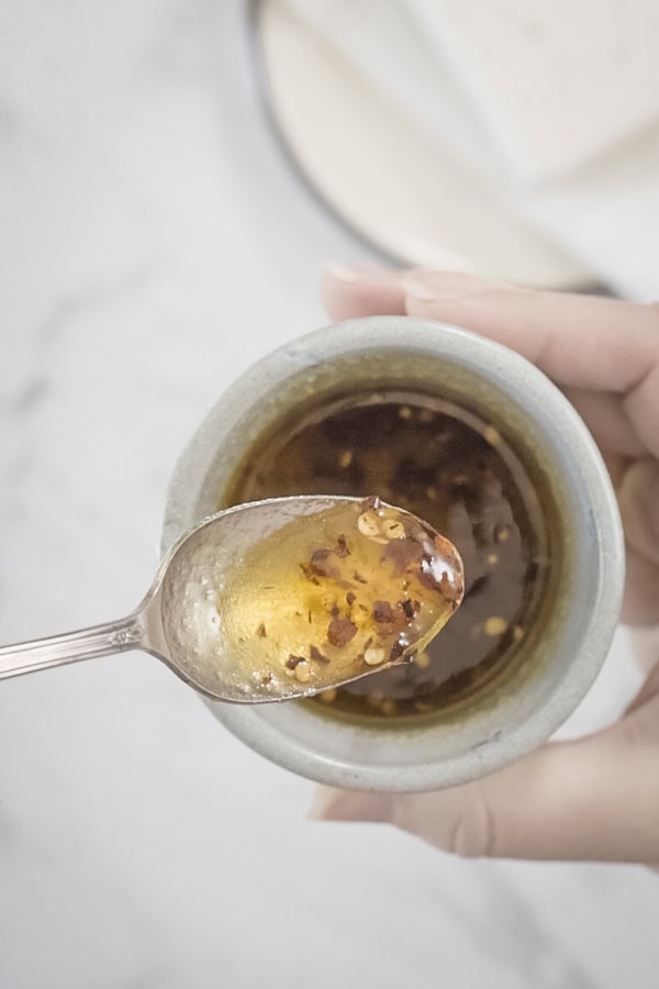 Spoonful of honey and red pepper flakes held over a bowl with the mixture inside.