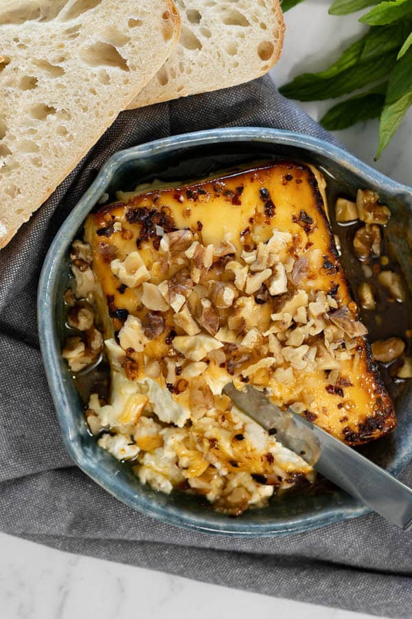 Baked feta topped with chopped walnuts in a dish, served with slices of crusty bread.