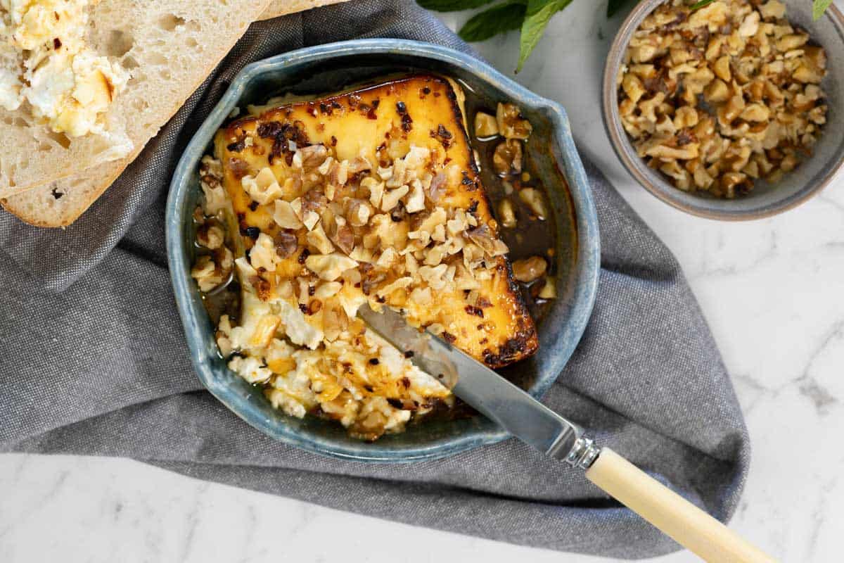 Golden baked feta topped with chopped walnuts and honey in a blue dish, served with crusty bread.