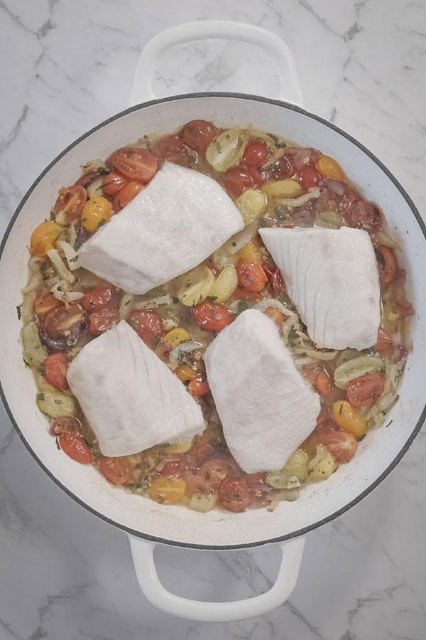 freshly roasted white fish in a baking dish, sitting on top of cherry tomatoes and fennel