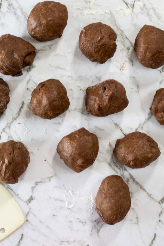 Chocolate dough cut into pieces for hot cross buns, on a marble counter.