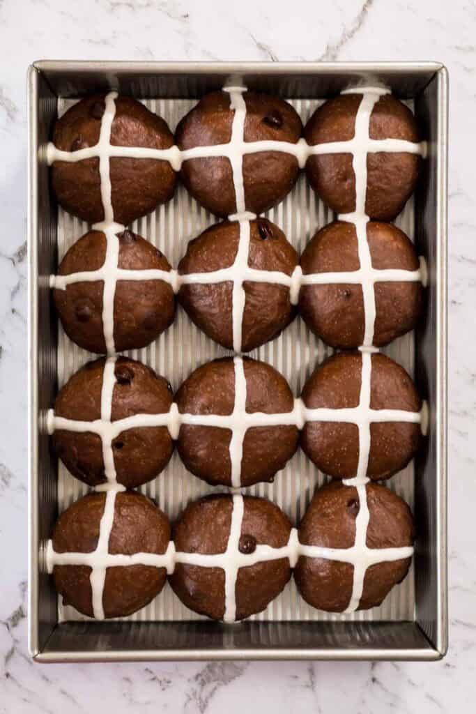 White crosses piped onto the tops of chocolate hot cross buns, ready to bake.
