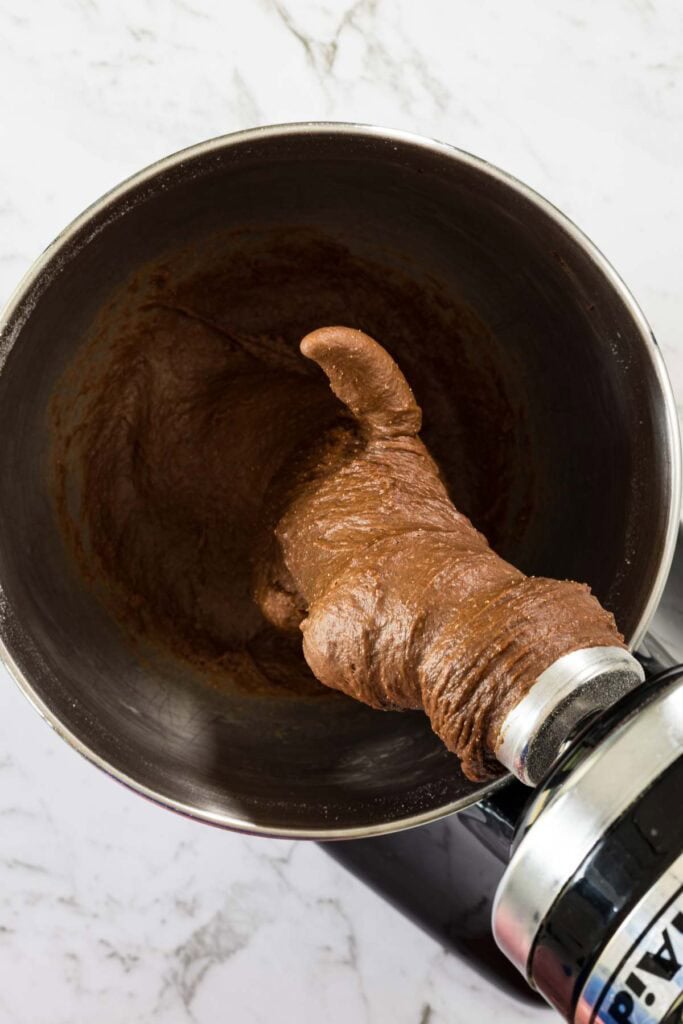 Mixed chocolate dough for milk bread hot cross buns, hanging from the dough hook of a mixer.