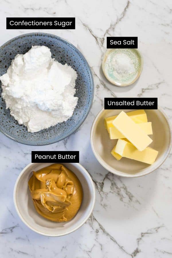 Overhead view of creamy peanut butter, sticks of butter, powdered sugar, and a small pinch of salt in separate bowls on a marble surface for chocolate and peanut butter brownies.