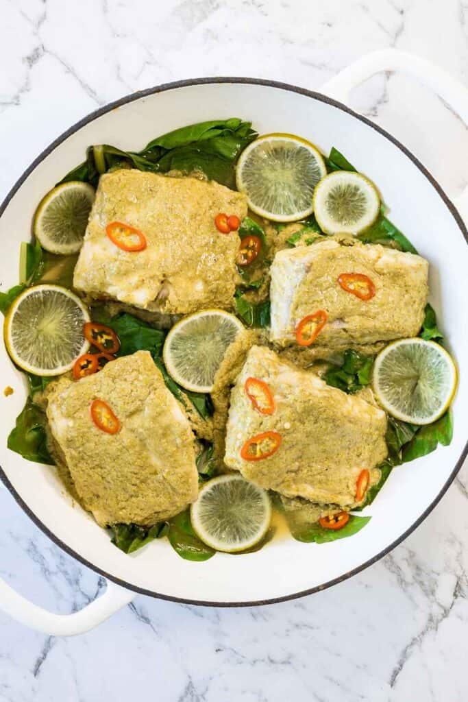 Freshly cooked coconut steamed fish with chilli and green vegetables, in a white enameled dish. 