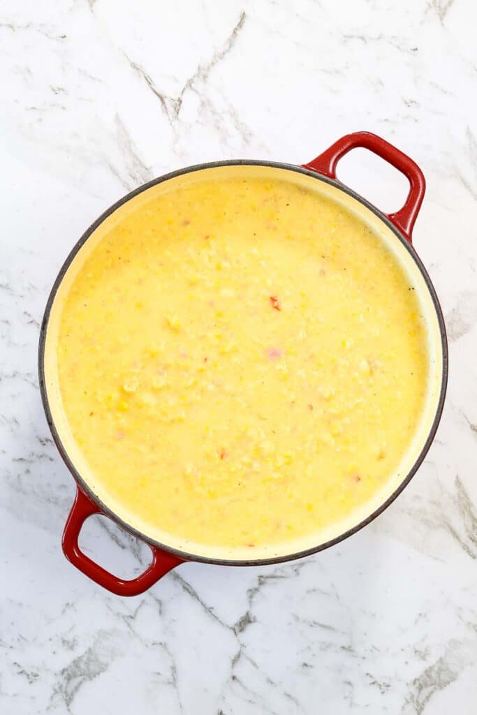The corn and bacon chowder is blended or creamed together inside the red enameled Dutch oven, taking on a smooth, velvety yellow appearance for corn and bacon chowder.