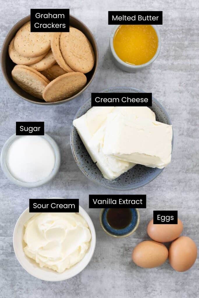 An overhead view of all ingredients—cream cheese blocks, eggs, vanilla extract, butter, round biscuits, heavy cream, and sugar—ready to be combined for the Creme Brulee Cheesecake base and filling.
