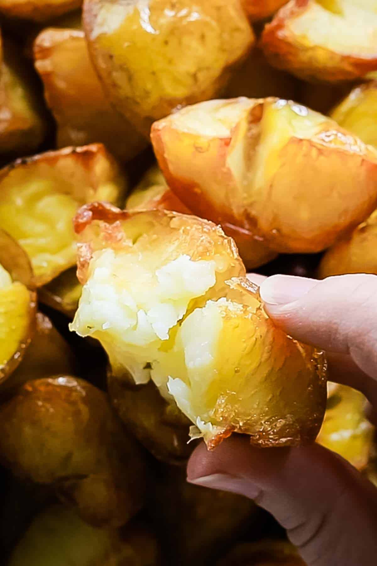 A big ceramic bowl of crispy roasted potatoes viewed from above. A hand can be seen underneath the bowl, holding it up to the camera.