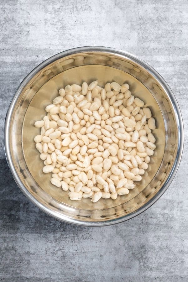 Soaked white beans in a stainless steel bowl with water.