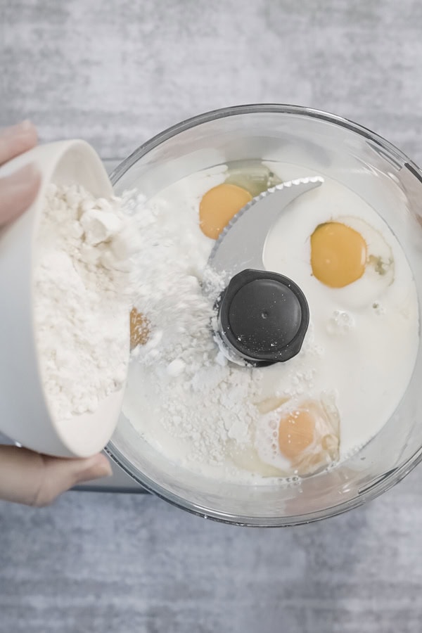Adding flour to a food processor with eggs and milk for Dutch Baby Pancake batter.