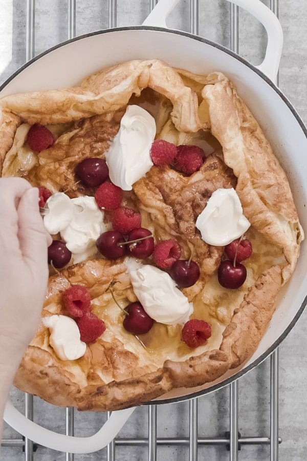 Topping Dutch Baby Pancake with cream, raspberries, and cherries.