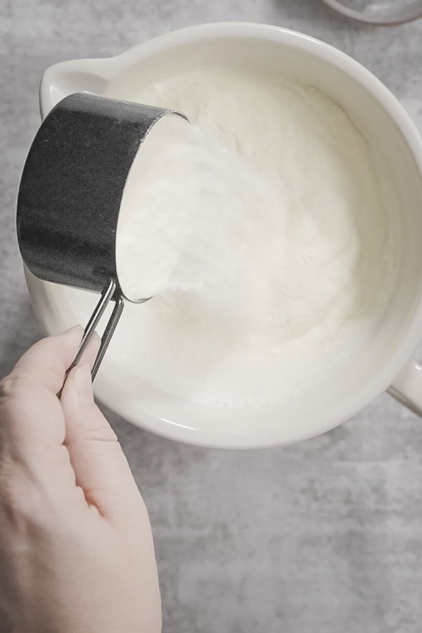 Pouring milk powder into a bowl of milk for homemade yogurt.