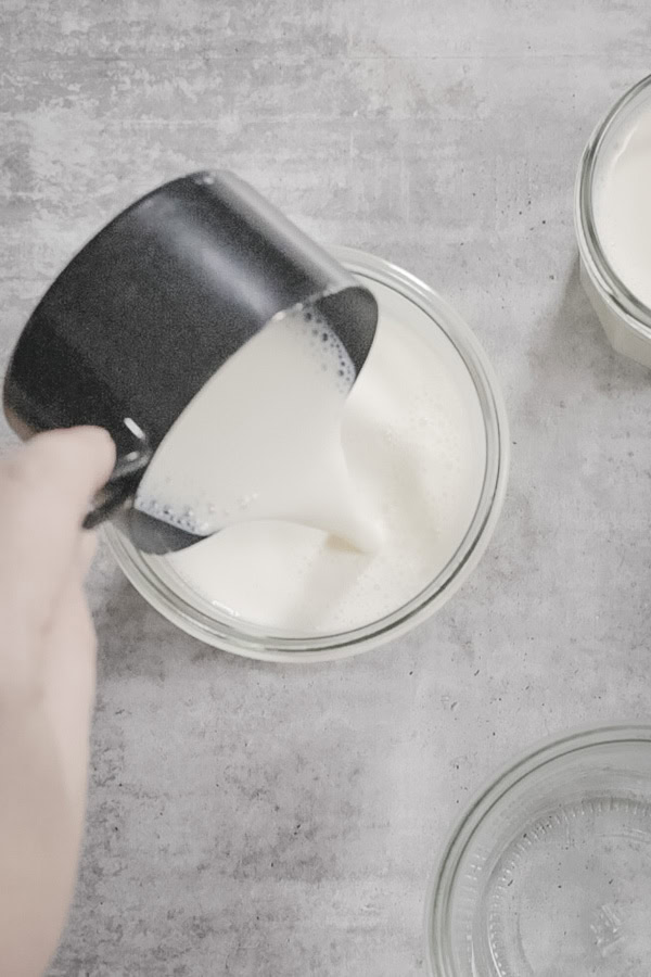 Pouring yogurt mixture into a glass jar from a measuring cup.