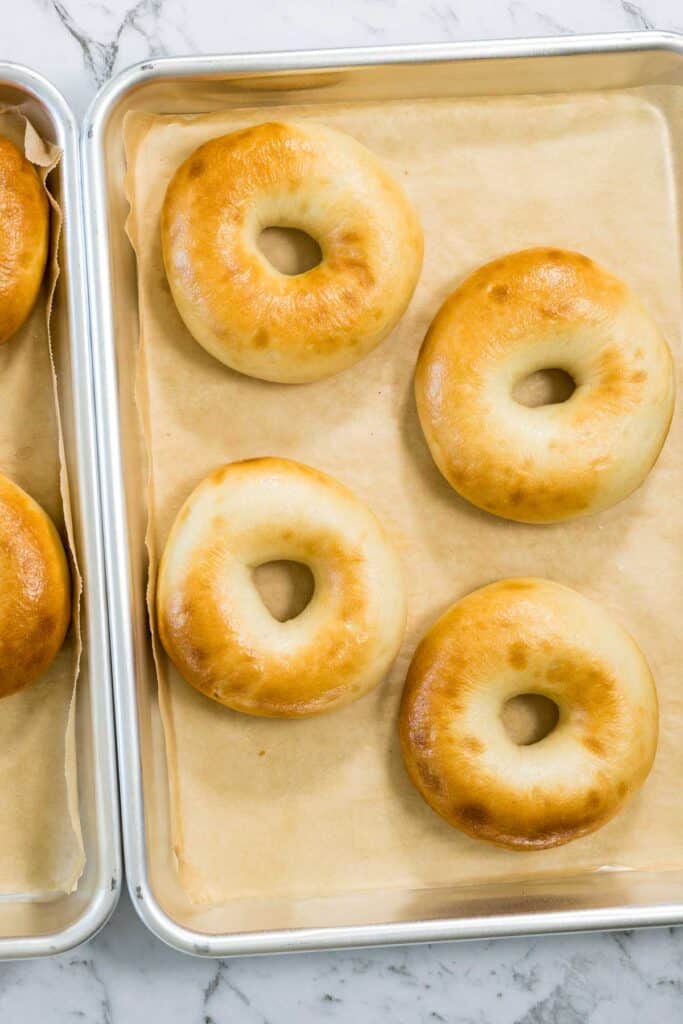 Freshly baked, golden-brown bagels with a glossy finish sit on parchment-lined silver baking sheets for zaatar bagels.