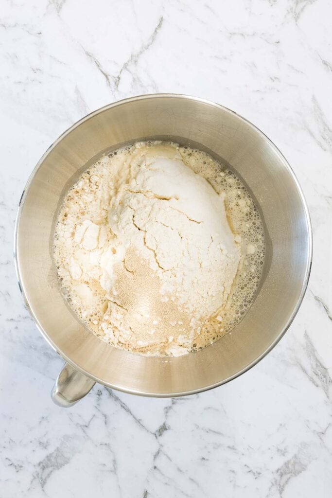 Dry flour and yeast sit in a pool of water and honey inside a stainless steel stand mixer bowl for zaatar bagels.