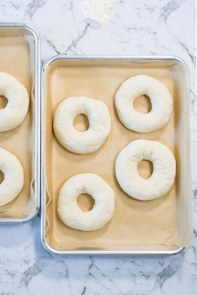 Shaped raw dough rings are placed on baking sheets lined with brown parchment paper for zaatar bagels.