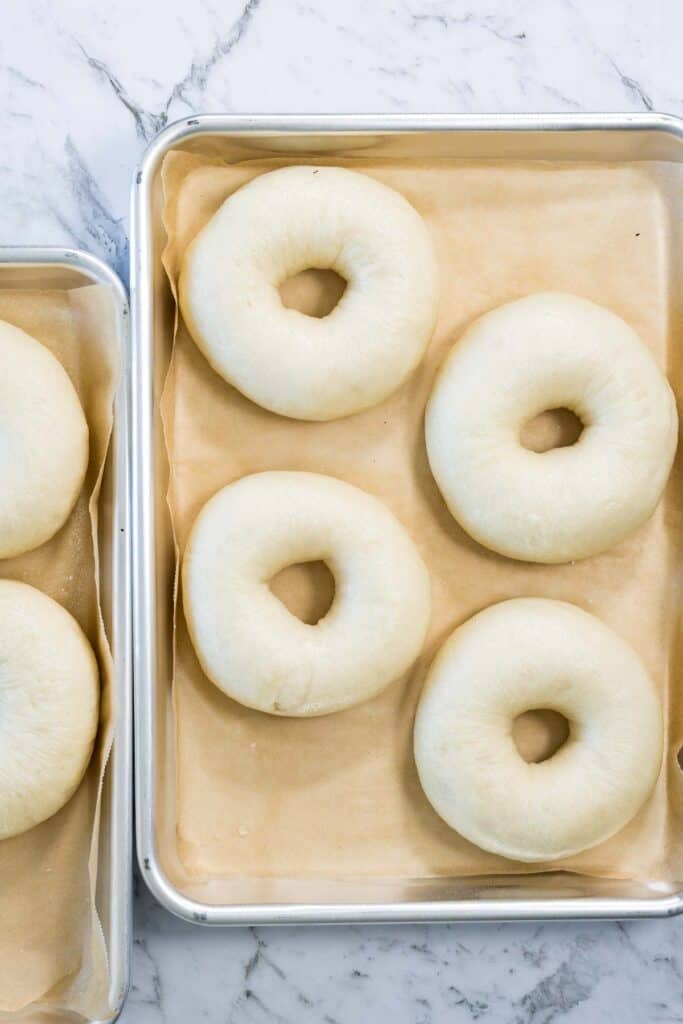 Smooth, puffed bagel dough rings sit on parchment-lined baking sheets after being boiled for zaatar bagels.