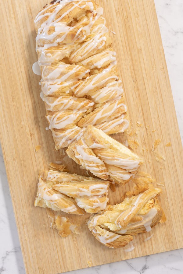 Sliced lemon cheesecake Danish with icing on a wooden board.