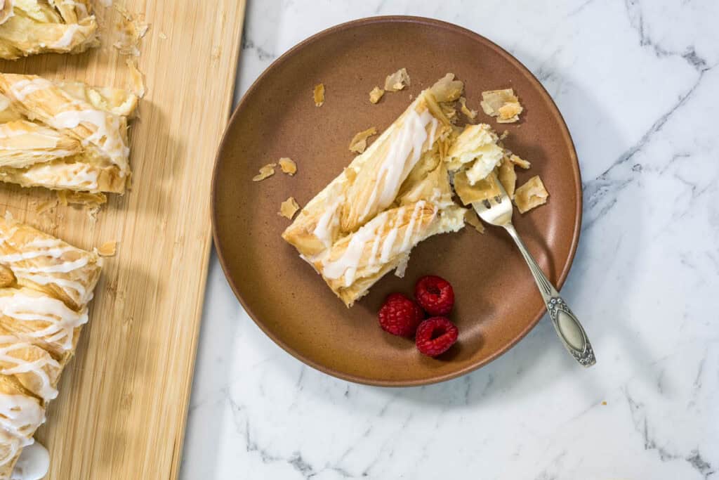 A slice of lemon cheesecake Danish on a plate with fresh raspberries.