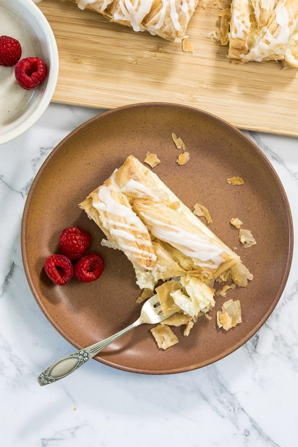 Lemon cheesecake Danish slice on a plate with a few raspberries and a forkful taken.