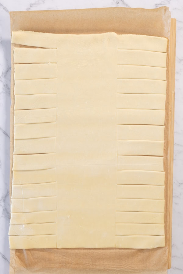 Puff pastry sheet with slits cut along both sides.