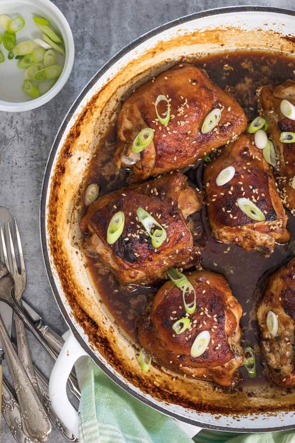 A roasting dish of freshly baked miso maple chicken, with a green tea towel and a pile of forks next to the dish. 