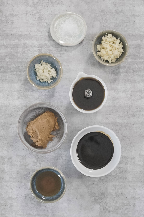 A series of small dishes containing marinade ingredients for miso maple roasted chicken. 
