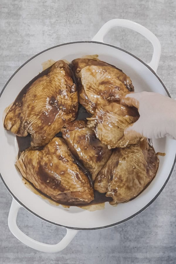 A hand turns chicken pieces in miso maple marinade, in a large white baking dish. 