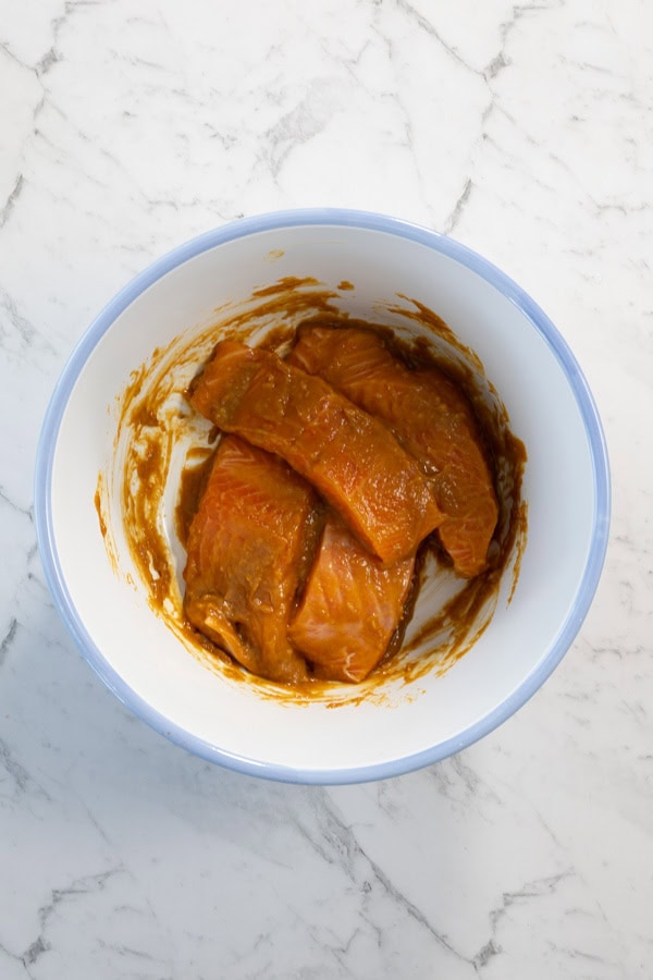 Salmon fillets coated in miso marinade inside a white bowl.