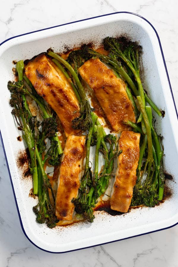 Golden roasted salmon and broccolini in a white enamel baking dish.