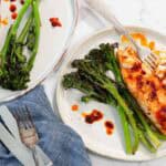 Two plates of roasted salmon with broccolini, topped with chili oil.