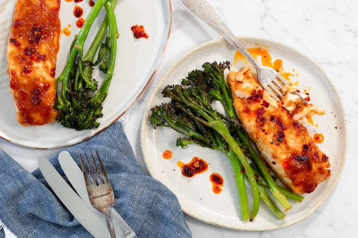 Two plates of roasted salmon with broccolini, topped with chili oil.
