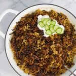 Lentil rice served in a white pot, topped with crispy onions, yogurt, and cucumber slices.