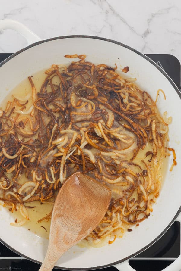 Crisping sliced onions in a white skillet with oil and a wooden spoon.