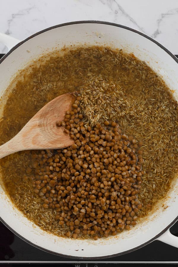 Lentils being stirred into a pot of seasoned rice and broth.