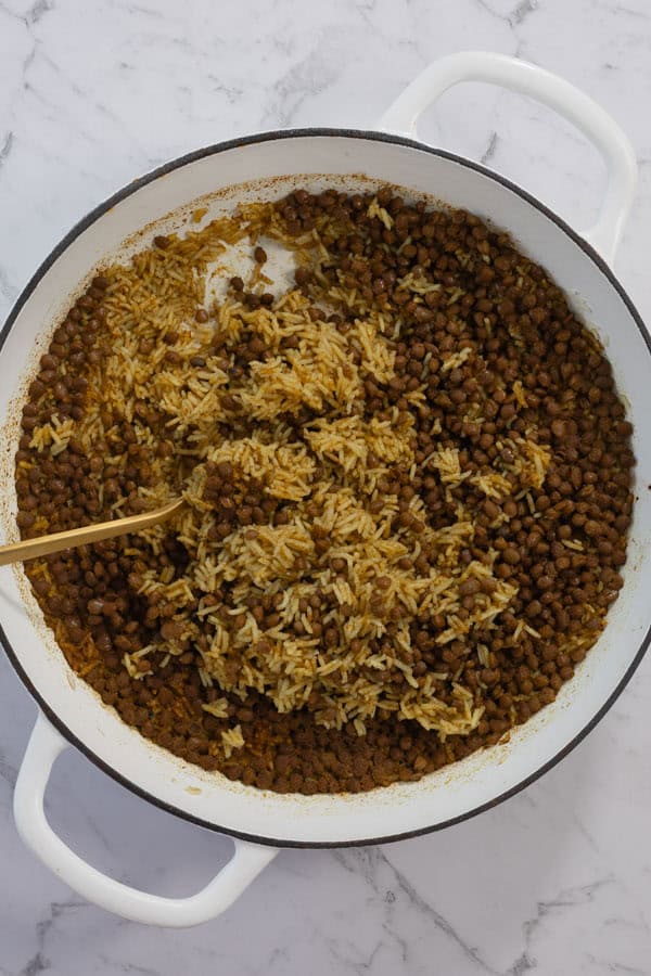 Cooked lentil rice being fluffed with a spoon in a white pot.