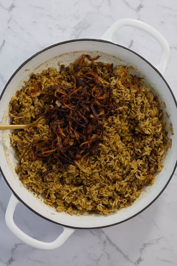 Fried onions added on top of spiced lentil rice in a white pot.