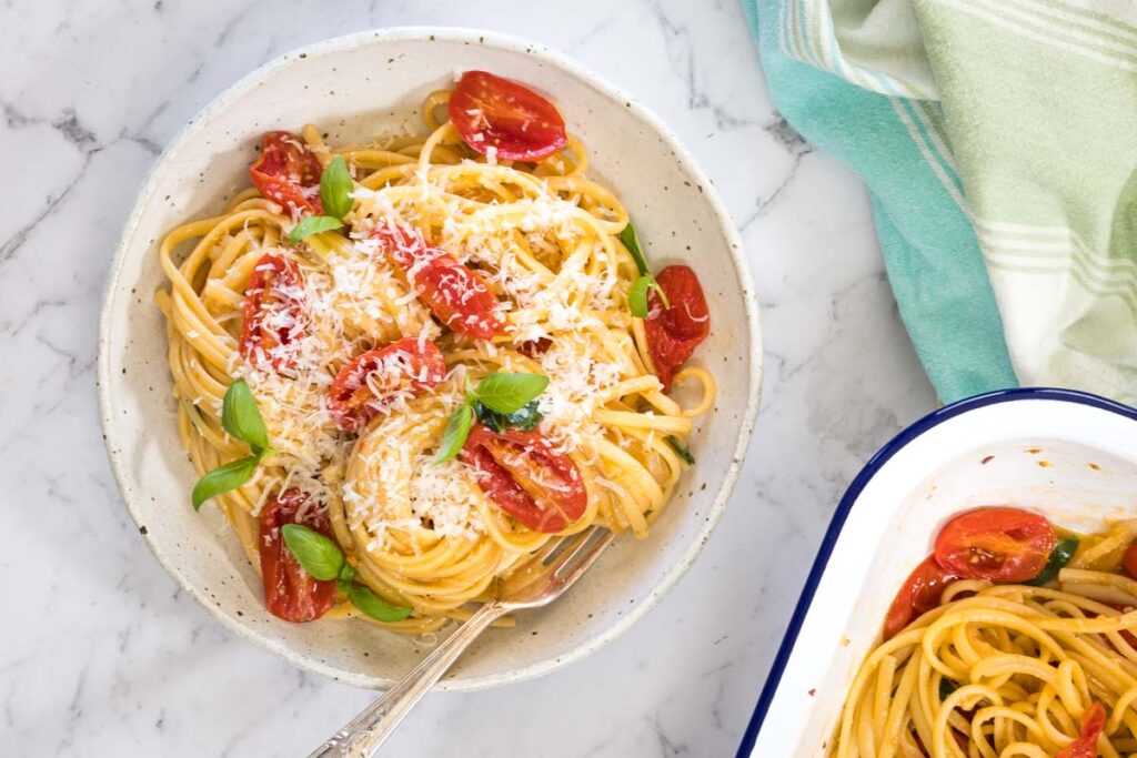 Top-down view of a ceramic bowl filled with steam oven pasta sits next to a green and white kitchen towel.