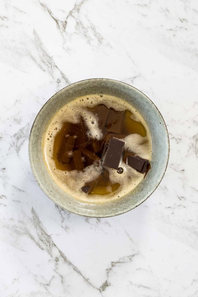Dark chocolate chunks sit partially submerged in a bowl of hot melted butter for chocolate and peanut butter brownies.