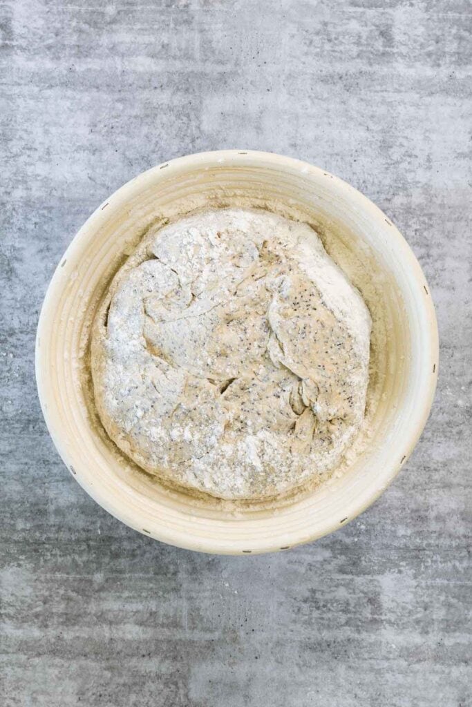 Poppy seed dough containing the potato filling, dusted heavily with flour, placed into a round, fluted banneton or proofing basket for its final rise before baking as potato and poppy seed bread.